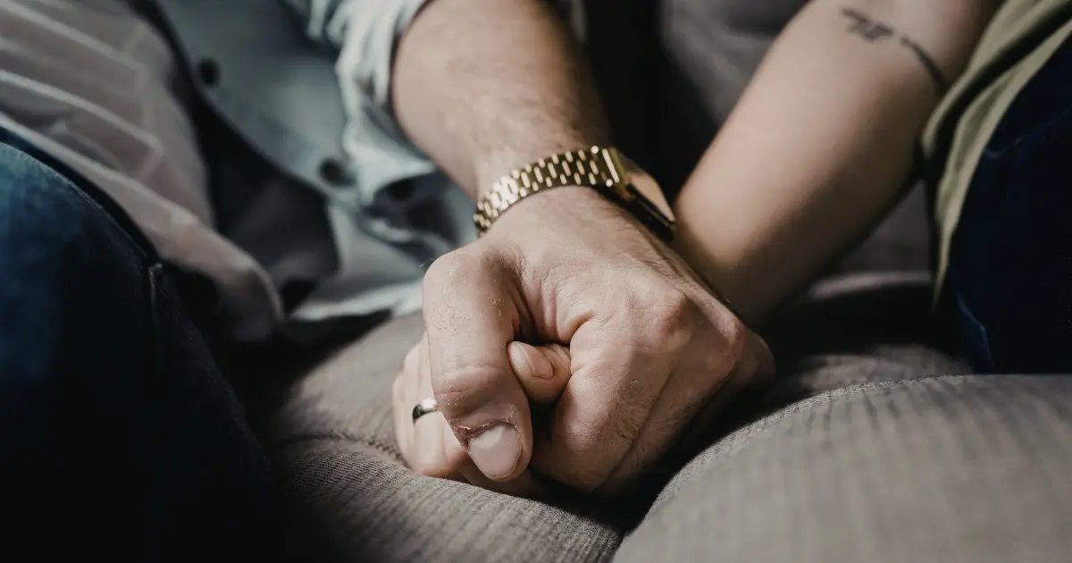 Two people hold hands on a couch, conveying affection and support.