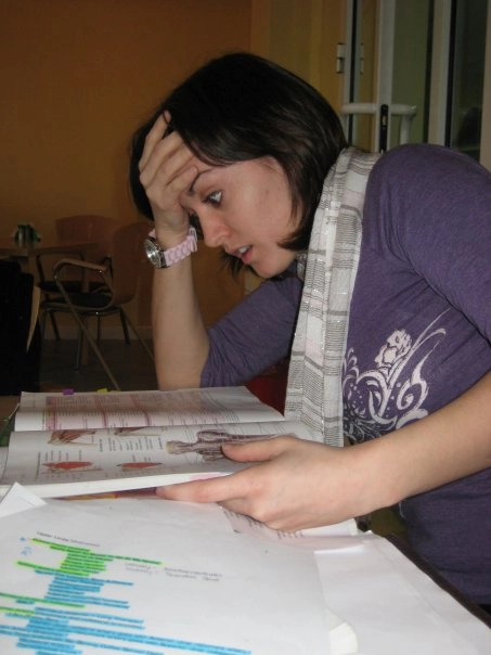 Study picture med school - Ann Marie MD Woman studying at a table, head in hand, looking stressed while reading a colorful report spread across papers.