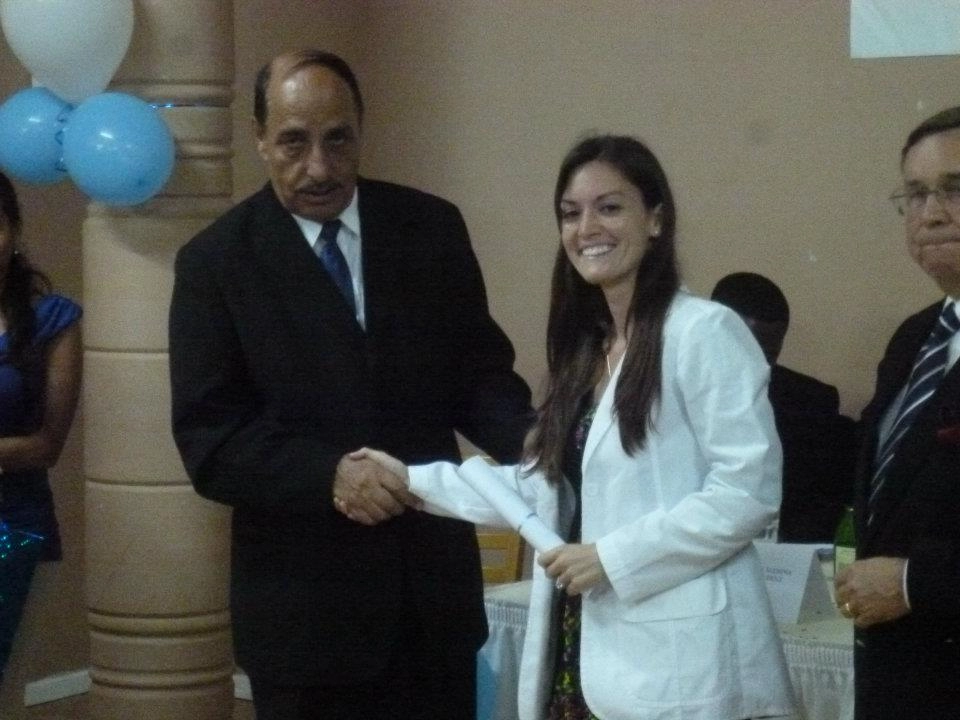 White Coat Ceremony - Ann Marie MD Two people shake hands at a formal event: a man in a suit and a smiling woman in a white lab coat, with balloons in the background.